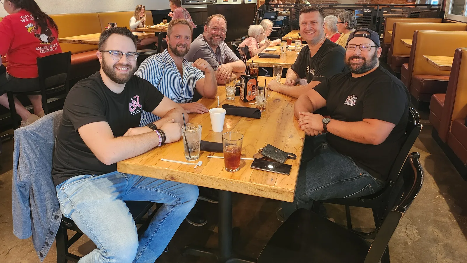 Five members of the MythWeaver team around a restaurant table, most of them in MythWeaver shirts, looking at the camera